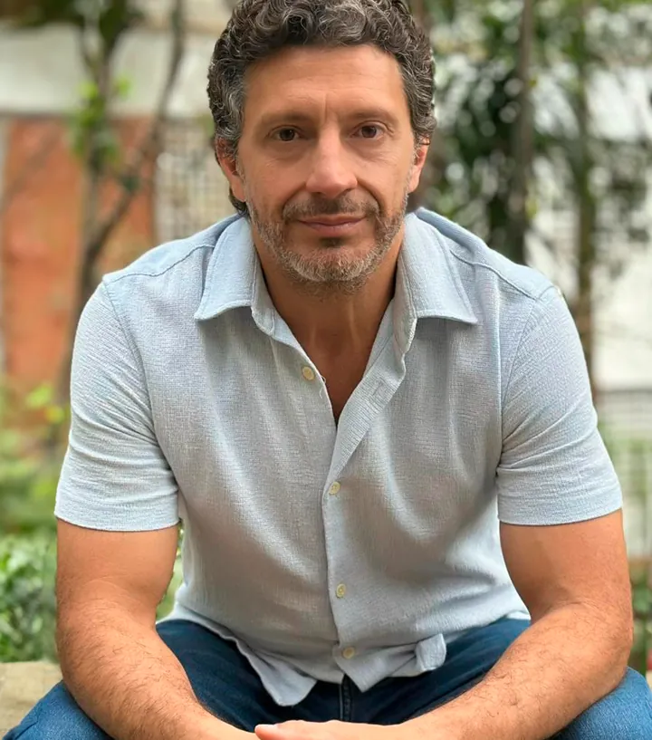 Frederico Ciongoli sentado num jardim, de camisa clara, olhando para a câmera